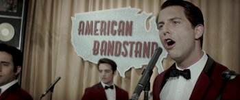 Movie still from “Jersey Boys” (2014), directed by Clint Eastwood – Two men are singing in front of an american bandstand sign; Medium shot, Over the shoulder angle