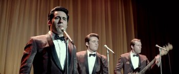 Movie still from “Jersey Boys” (2014), directed by Clint Eastwood – A group of men standing next to each other on a stage with microphones; Medium shot, High angle