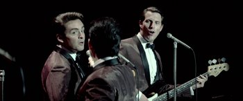 Movie still from “Jersey Boys” (2014), directed by Clint Eastwood – A group of men standing next to each other on a stage; Medium shot, Over the shoulder angle