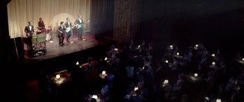 Movie still from “Jersey Boys” (2014), directed by Clint Eastwood – A crowd of people sitting on a stage and a man playing a guitar; Extreme Wide shot, High angle