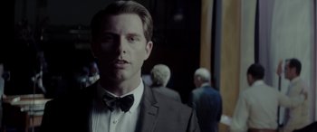 Movie still from “Jersey Boys” (2014), directed by Clint Eastwood – A man in a suit and bow tie standing in front of other people; Close Up shot, Over the shoulder angle