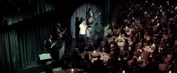 Movie still from “Jersey Boys” (2014), directed by Clint Eastwood – A group of people sitting at a table playing instruments; Extreme Wide shot, High angle