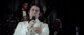 Movie still from “Jersey Boys” (2014), directed by Clint Eastwood – A man in a white shirt and bow tie holding a microphone; Close Up shot, Over the shoulder angle