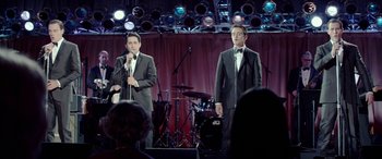 Movie still from “Jersey Boys” (2014), directed by Clint Eastwood – A couple of men standing on top of a stage next to each other; Wide shot, Over the shoulder angle