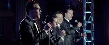 Movie still from “Jersey Boys” (2014), directed by Clint Eastwood – A group of men in tuxedos singing into microphones; Medium shot, High angle