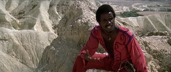 Movie still from “Jesus Christ Superstar” (1973), directed by Norman Jewison – A man in a red shirt sitting on top of a hill; Medium shot, Low angle