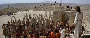 Movie still from “Jesus Christ Superstar” (1973), directed by Norman Jewison – A group of people gathered in the desert with palm fronds; Extreme Wide shot, High angle