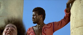 Movie still from “Jesus Christ Superstar” (1973), directed by Norman Jewison – A man in a pink shirt is standing in front of a blue sky; Close Up shot, Low angle