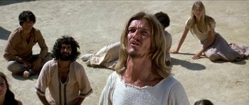 Movie still from “Jesus Christ Superstar” (1973), directed by Norman Jewison – A man with long blonde hair and no shirt is sitting on the ground; Close Up shot, Low angle