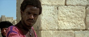 Movie still from “Jesus Christ Superstar” (1973), directed by Norman Jewison – A person wearing a necklace near a stone wall; Close Up shot, Low angle