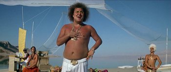 Movie still from “Jesus Christ Superstar” (1973), directed by Norman Jewison – A man in a white shirt and white shorts on the beach; Medium shot, Low angle