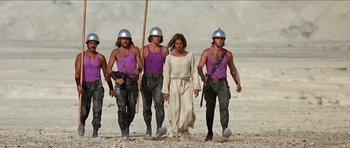 Movie still from “Jesus Christ Superstar” (1973), directed by Norman Jewison – A group of men in purple shirts are leading a man in a white dress; Wide shot, Low angle
