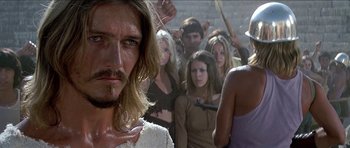 Movie still from “Jesus Christ Superstar” (1973), directed by Norman Jewison – A group of people standing around a man with long blonde hair; Close Up shot, Over the shoulder angle