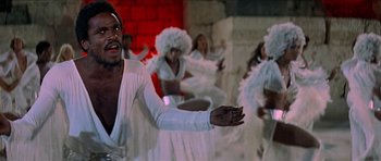 Movie still from “Jesus Christ Superstar” (1973), directed by Norman Jewison – A group of people dressed in white dancing in front of a brick wall; Medium shot, Low angle