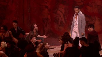 Movie still from “Jesus Christ Superstar Live in Concert” (2018), directed by Alex Rudzinski – A group of people sitting on the ground; Wide shot, Over the shoulder angle