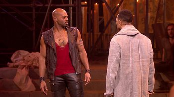 Movie still from “Jesus Christ Superstar Live in Concert” (2018), directed by Alex Rudzinski – A man in a red shirt and a man in a leather vest; Medium shot, Over the shoulder angle