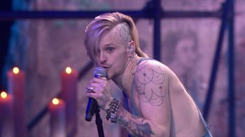 Movie still from “Jesus Christ Superstar Live in Concert” (2018), directed by Alex Rudzinski – A man with tattoos is singing into a microphone; Medium shot, Over the shoulder angle