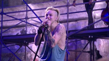 Movie still from “Jesus Christ Superstar Live in Concert” (2018), directed by Alex Rudzinski – A man with tattoos is singing into a microphone; Medium shot, Over the shoulder angle