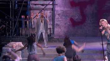 Movie still from “Jesus Christ Superstar Live in Concert” (2018), directed by Alex Rudzinski – A group of people are dancing in front of a man; Wide shot, Over the shoulder angle