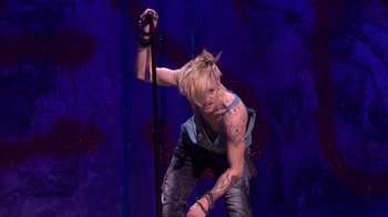 Movie still from “Jesus Christ Superstar Live in Concert” (2018), directed by Alex Rudzinski – A man with a tattoo on his arm is holding a microphone; Medium shot, Low angle