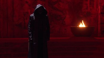 Movie still from “Jesus Christ Superstar Live in Concert” (2018), directed by Alex Rudzinski – A man in a black coat standing in front of a fire pit; Wide shot, Over the shoulder angle