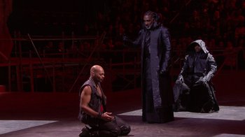 Movie still from “Jesus Christ Superstar Live in Concert” (2018), directed by Alex Rudzinski – A man in a long black coat and a man in a black robe; Wide shot, Over the shoulder angle
