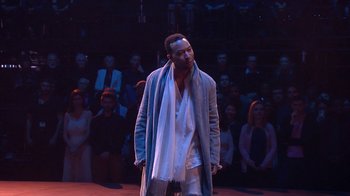 Movie still from “Jesus Christ Superstar Live in Concert” (2018), directed by Alex Rudzinski – A man standing in front of an audience on a stage; Medium shot, Over the shoulder angle