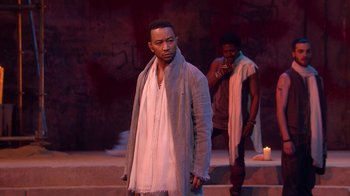 Movie still from “Jesus Christ Superstar Live in Concert” (2018), directed by Alex Rudzinski – A man standing in front of another man on a stage; Medium shot, Over the shoulder angle