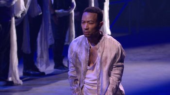 Movie still from “Jesus Christ Superstar Live in Concert” (2018), directed by Alex Rudzinski – A man standing on a stage wearing a white shirt; Medium shot, High angle