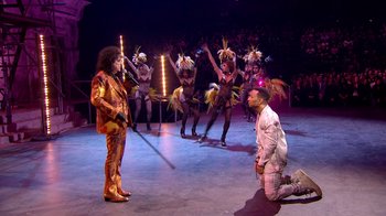 Movie still from “Jesus Christ Superstar Live in Concert” (2018), directed by Alex Rudzinski – A man kneeling down next to a woman on a stage; Wide shot, High angle