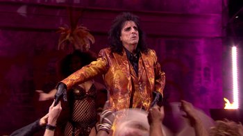 Movie still from “Jesus Christ Superstar Live in Concert” (2018), directed by Alex Rudzinski – A man in a red and yellow jacket standing in front of a crowd; Medium shot, Over the shoulder angle