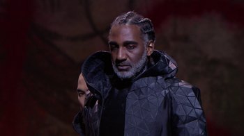 Movie still from “Jesus Christ Superstar Live in Concert” (2018), directed by Alex Rudzinski – A man in a black jacket is standing in a dark room; Close Up shot, Low angle