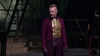 Movie still from “Jesus Christ Superstar Live in Concert” (2018), directed by Alex Rudzinski – A man in a purple jacket and purple pants; Medium shot, Over the shoulder angle