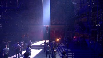 Movie still from “Jesus Christ Superstar Live in Concert” (2018), directed by Alex Rudzinski – A group of people standing around a stage with a crucifixion; Extreme Wide shot, Low angle