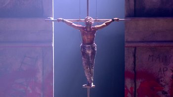 Movie still from “Jesus Christ Superstar Live in Concert” (2018), directed by Alex Rudzinski – A man hanging from a cross in a dark room; Wide shot, Low angle