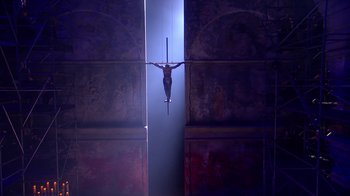 Movie still from “Jesus Christ Superstar Live in Concert” (2018), directed by Alex Rudzinski – A man hanging upside down on a pole in a dark room; Extreme Wide shot, Low angle