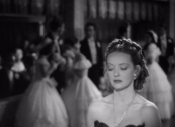 Movie still from “Jezebel” (1938), directed by William Wyler – A woman in a black dress is standing in front of a group of people; Close Up shot, High angle