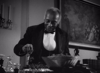 Movie still from “Jezebel” (1938), directed by William Wyler – An older man in a suit and bow tie cutting a cake; Medium shot, Low angle