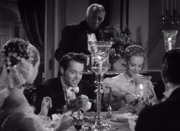 Movie still from “Jezebel” (1938), directed by William Wyler – A group of people sitting around a table with candles; Medium shot, High angle