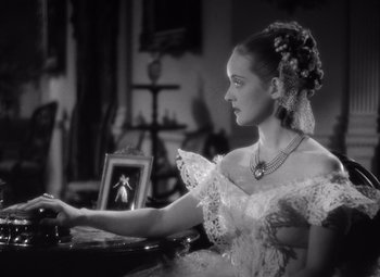 Movie still from “Jezebel” (1938), directed by William Wyler – A woman in a white dress sitting in front of a mirror; Medium shot, High angle