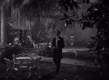 Movie still from “Jezebel” (1938), directed by William Wyler – A black and white photo of a man standing in a garden; Wide shot, High angle