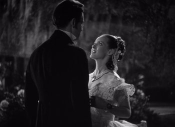 Movie still from “Jezebel” (1938), directed by William Wyler – A man and a woman standing next to each other in front of a tree; Medium shot, Low angle