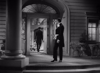 Movie still from “Jezebel” (1938), directed by William Wyler – A man in a suit standing in front of a building; Wide shot, Over the shoulder angle