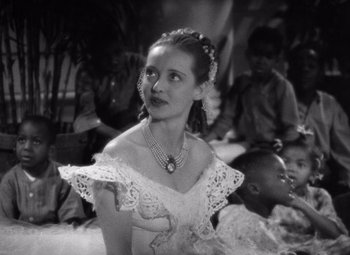 Movie still from “Jezebel” (1938), directed by William Wyler – A woman in a white dress is sitting in front of a group of people; Close Up shot, High angle