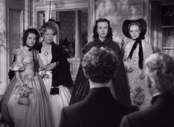 Movie still from “Jezebel” (1938), directed by William Wyler – A group of people in period clothing standing in front of a man; Medium shot, Over the shoulder angle