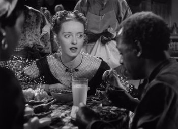 Movie still from “Jezebel” (1938), directed by William Wyler – A woman sitting at a table with a glass of milk; Medium shot, High angle