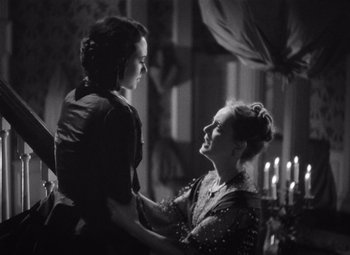 Movie still from “Jezebel” (1938), directed by William Wyler – A woman and a child are holding each other in front of candles in a room; Medium shot, Over the shoulder angle