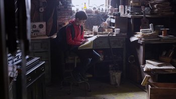 Movie still from “Turkey Hollow” (2015), directed by Kirk R. Thatcher – A person sitting at a desk in a room; Wide shot, Low angle