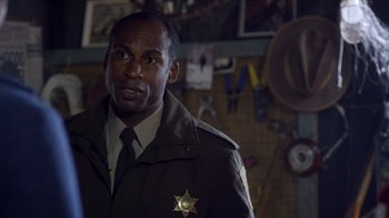 Movie still from “Turkey Hollow” (2015), directed by Kirk R. Thatcher – A man in a sheriff's uniform standing in front of a wall; Close Up shot, Over the shoulder angle