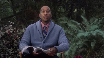 Movie still from “Turkey Hollow” (2015), directed by Kirk R. Thatcher – A man sitting in a chair holding a book; Medium shot, Low angle